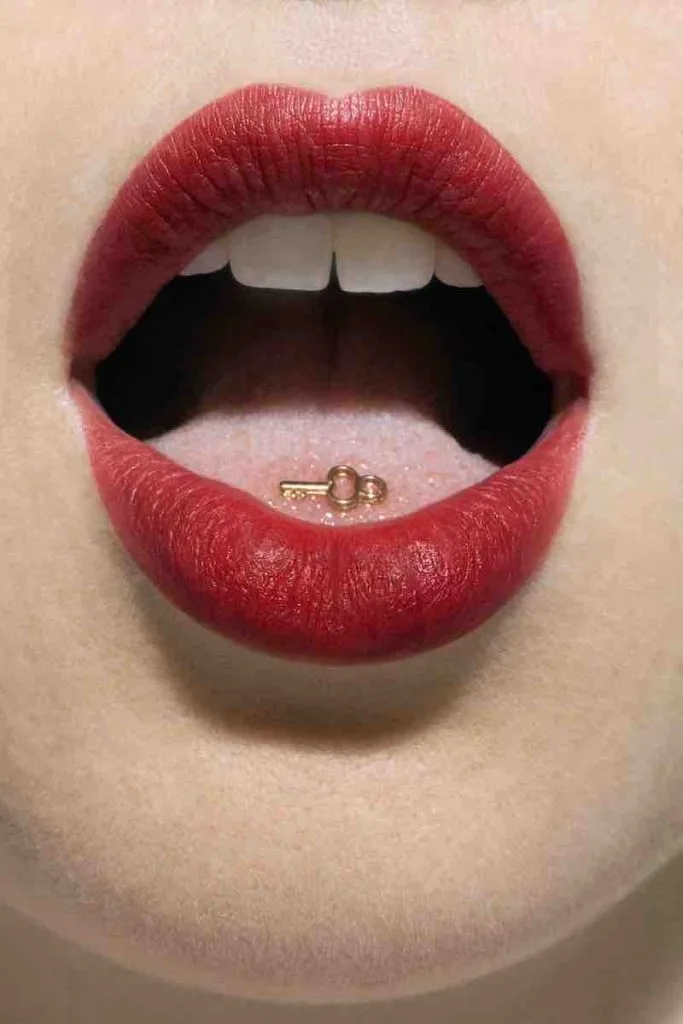 A model wears red lipstick and has her mouth open revealing a small gold on her tongue for a photoshoot in Hudson New York.